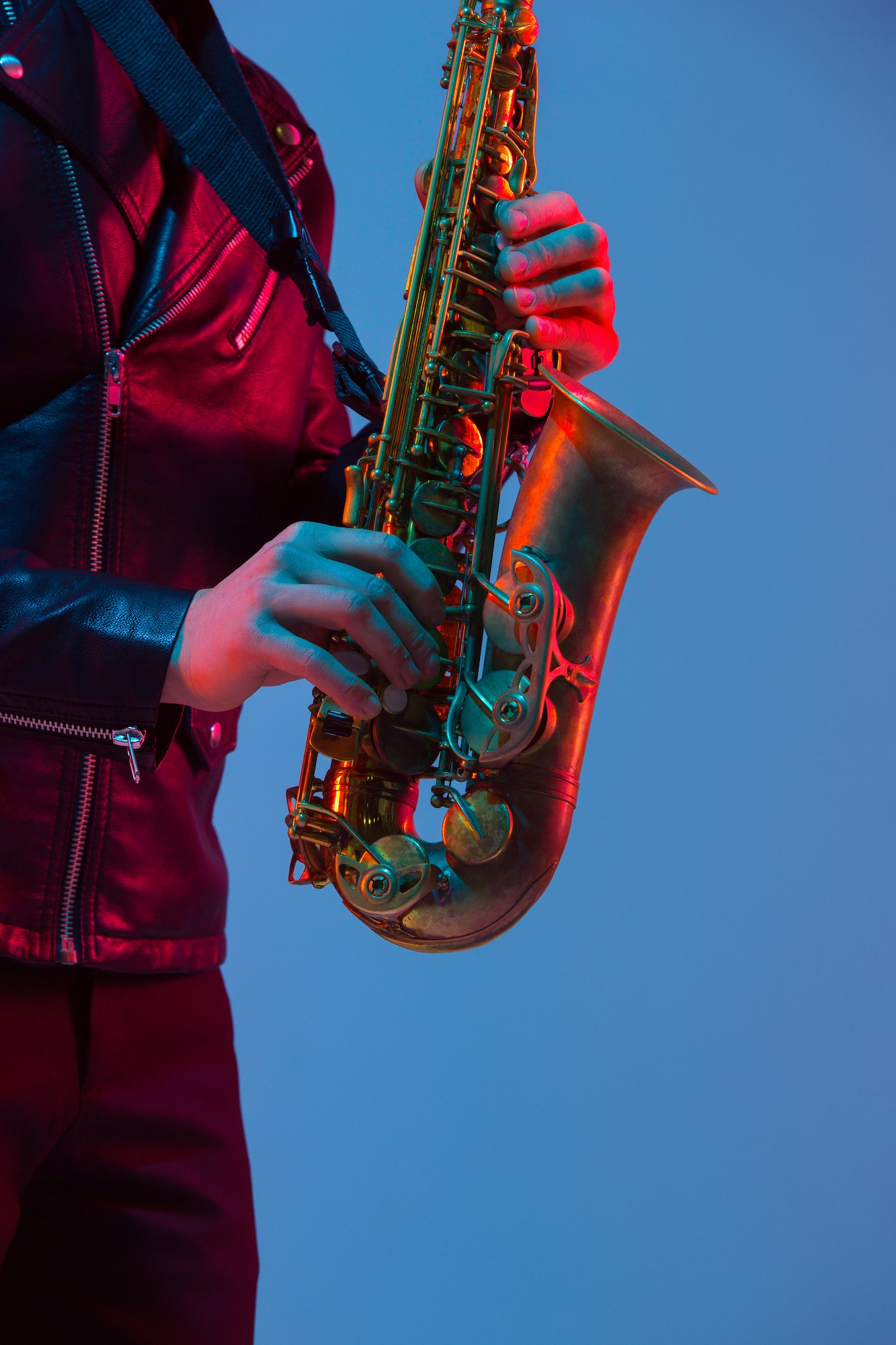 Young caucasian jazz musician playing the saxophone in neon light, close up